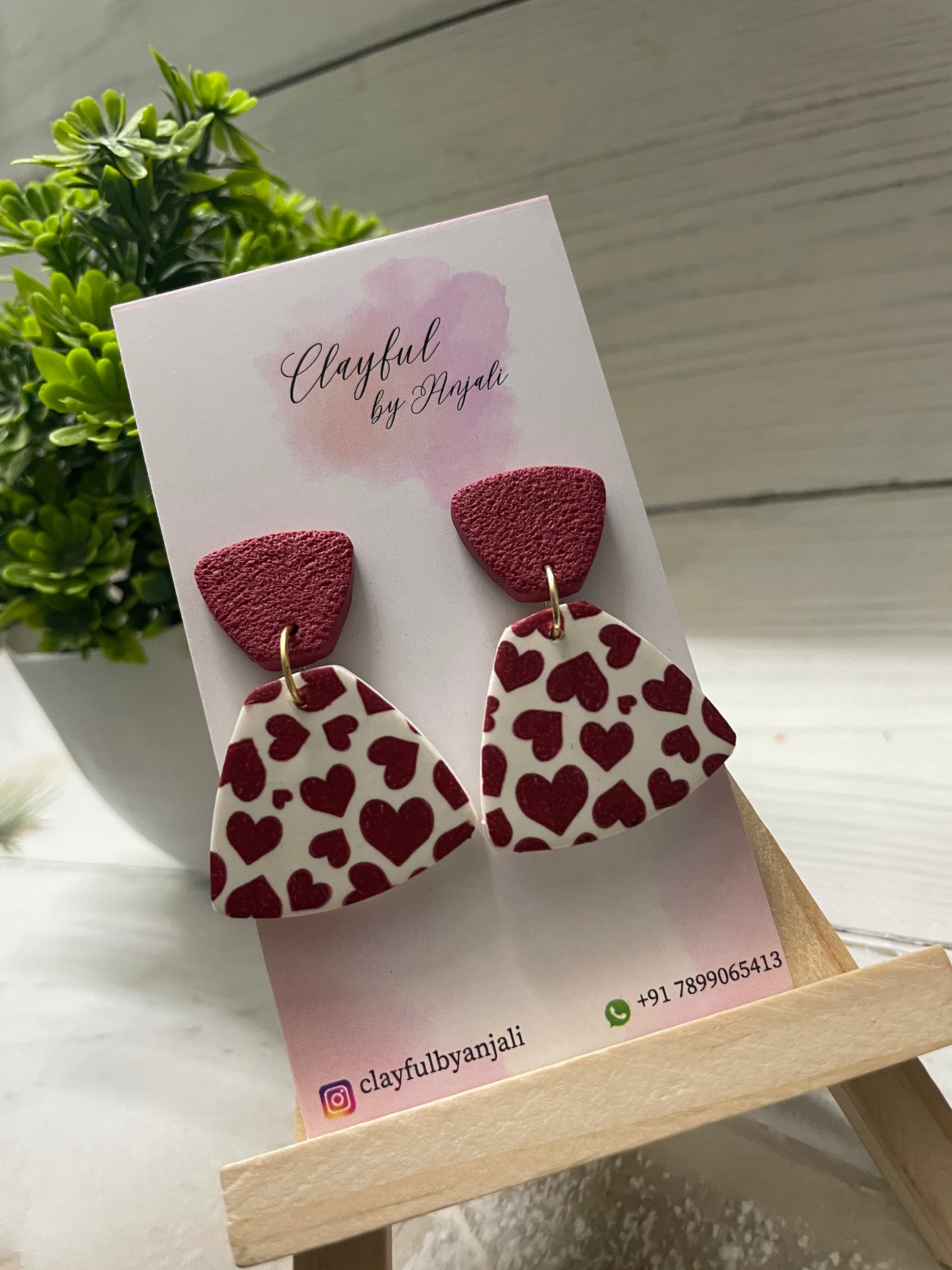 Handcrafted clay earrings with a burgundy heart transfer sheet pattern on a white fan-shaped drop, paired with a textured burgundy top.