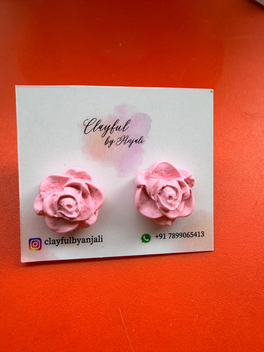 Pink rose-shaped earrings on a white card with branding text, placed on an orange surface.
