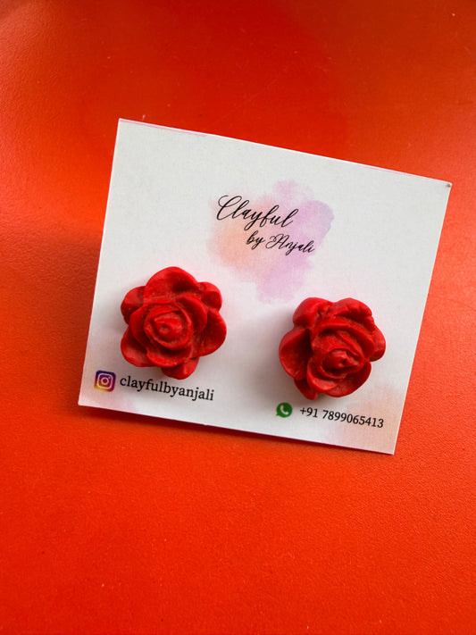 Red rose-shaped earrings on a white card with branding details against an orange background