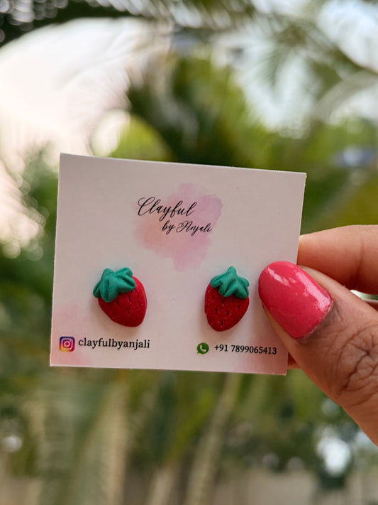 Strawberry-shaped studs held against a blurred green background.
