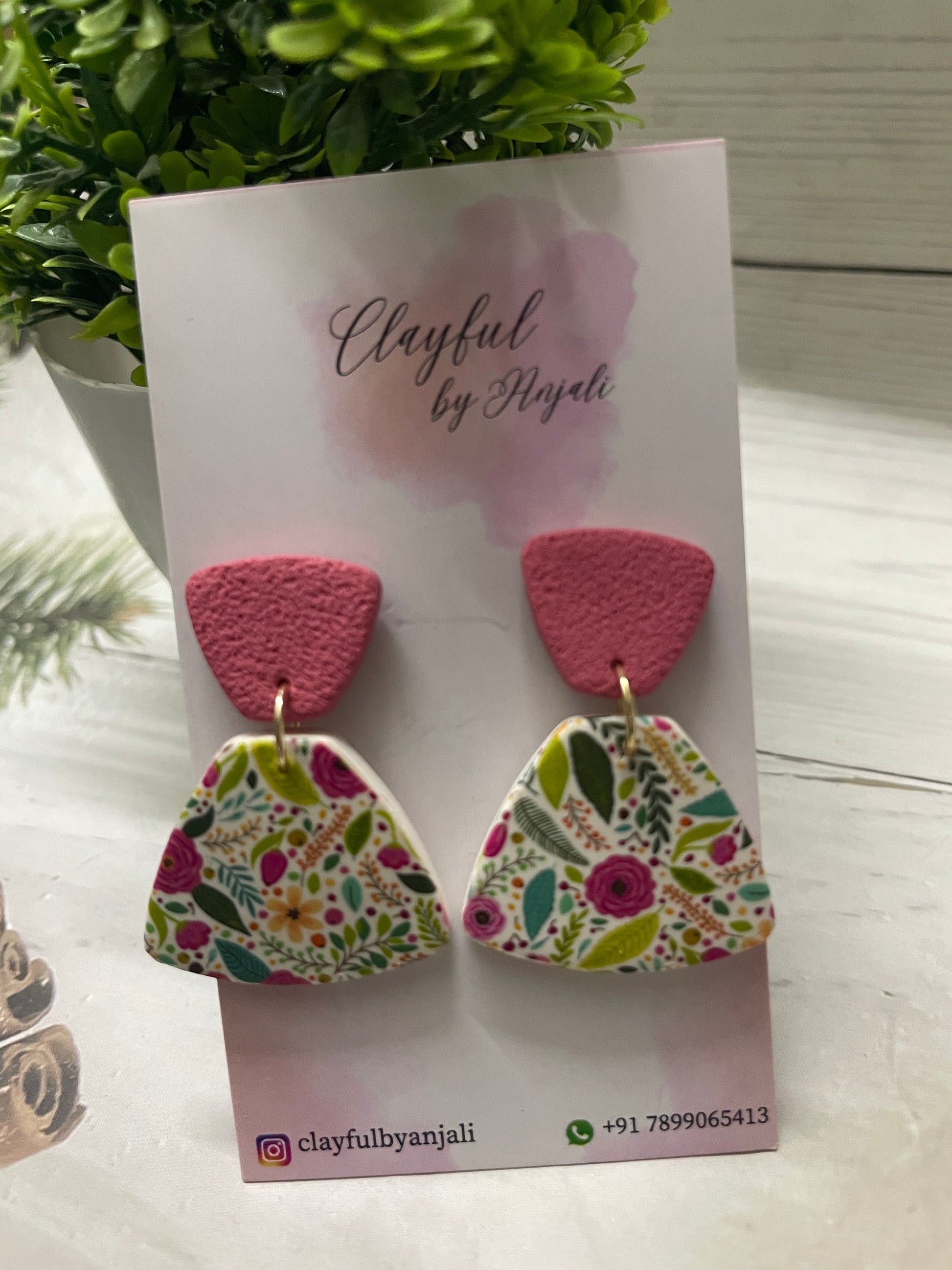 Handcrafted polymer clay earrings named Meadow Bloom, featuring a colorful wildflower transfer sheet pattern on a fan-shaped base with a textured rose-pink top