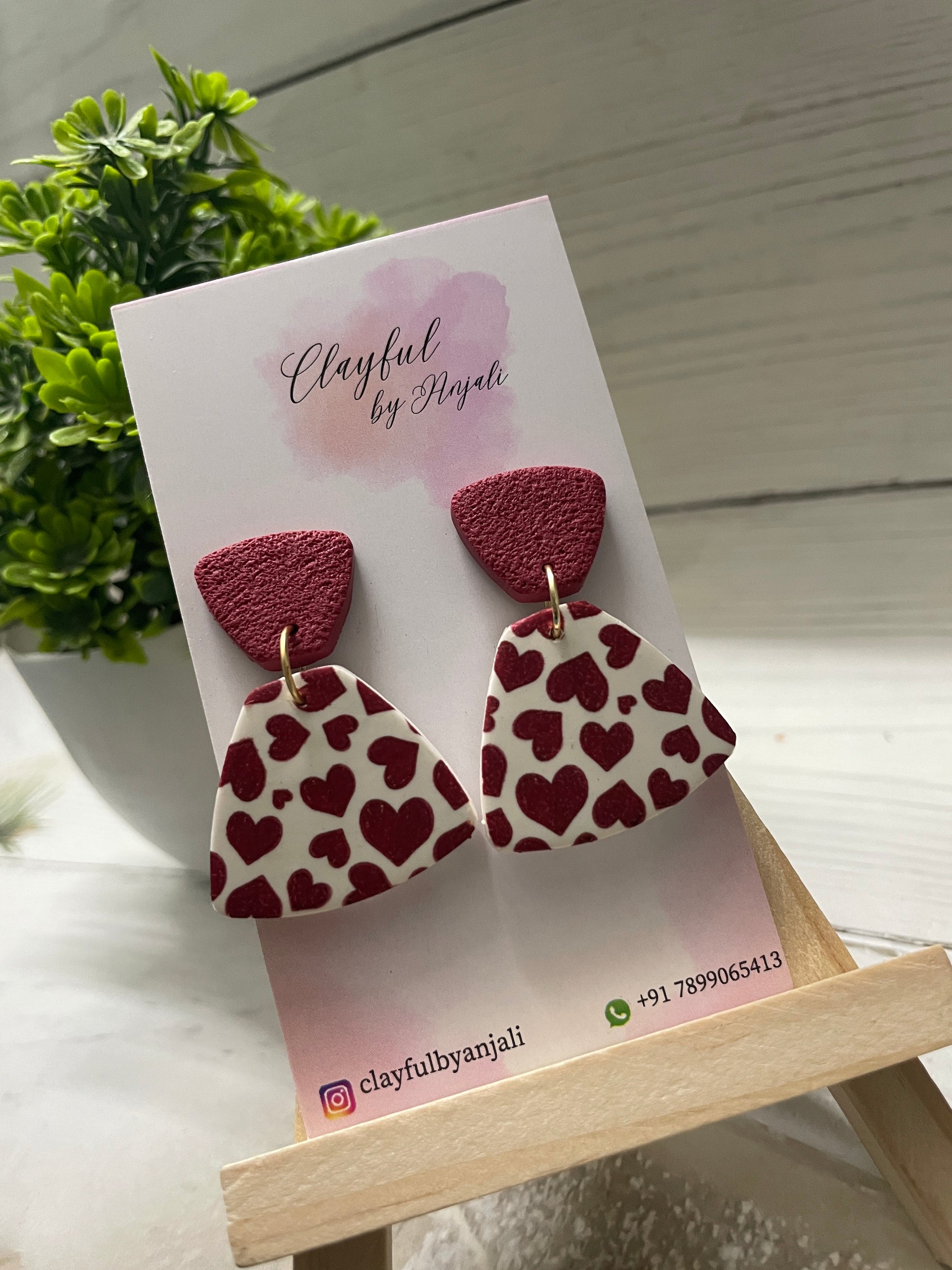 Handcrafted clay earrings with a burgundy heart transfer sheet pattern on a white fan-shaped drop, paired with a textured burgundy top.